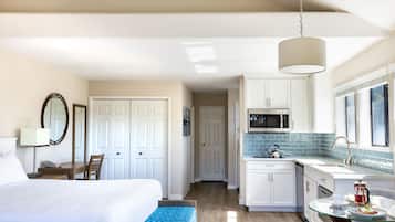 A hotel room with a bed, bedside table, lamp, and a view of the kitchen area.