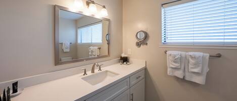 A bathroom with a large mirror, a sink, and a window with blinds.