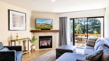 Una sala de estar moderna con chimenea, televisor de pantalla plana, sofá y balcón con vistas a árboles.
