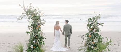 Ett par som promenerar hand i hand på en strand med blomsterdekorerade valv.