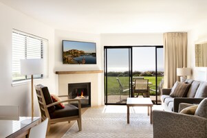 Una sala de estar con chimenea, sofá, mesa de comedor y vistas a un paisaje verde a través de amplios ventanales.