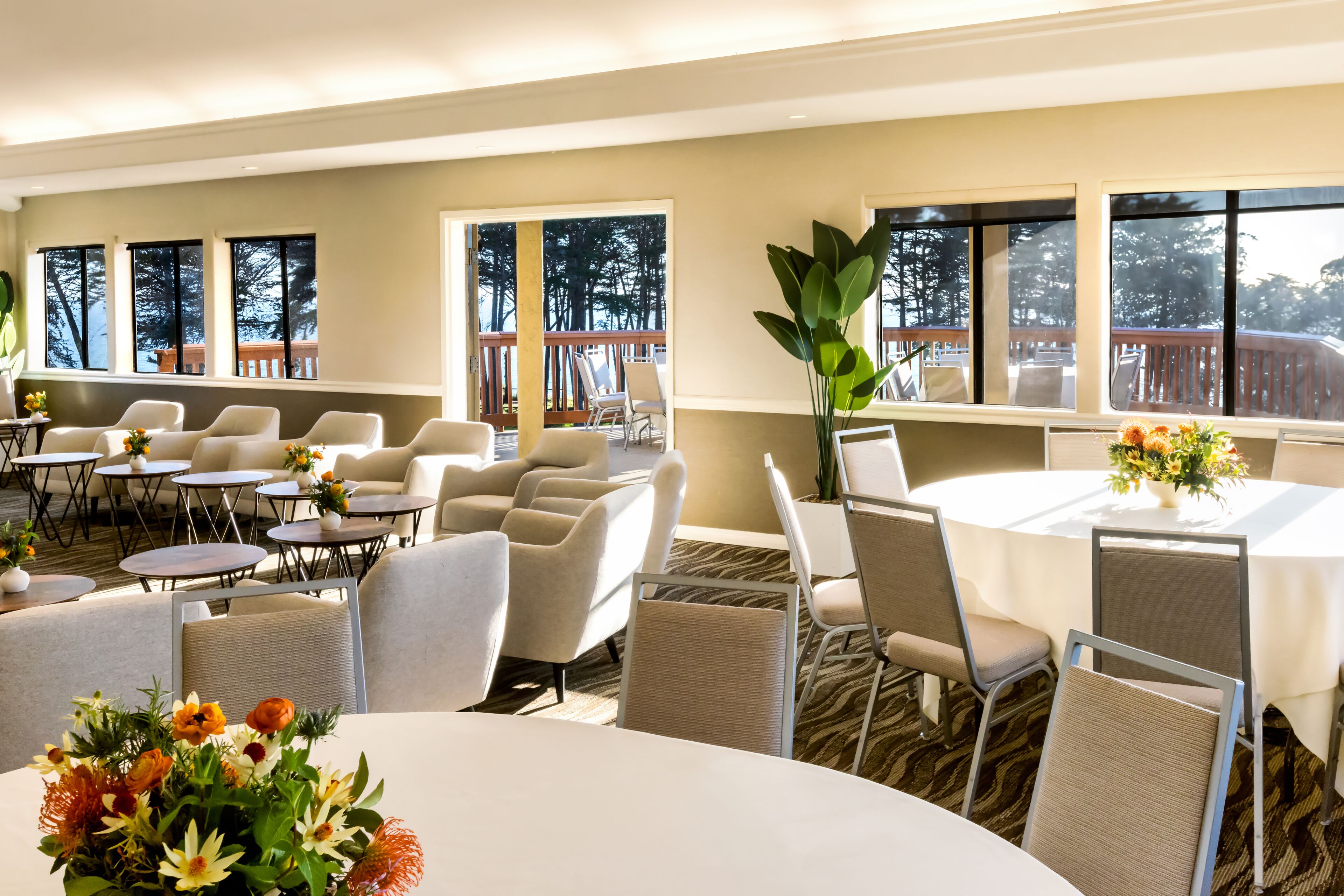 Habitación de hotel con un ventanal grande, zona de comedor con mesas y sillas redondas y vistas al exterior.