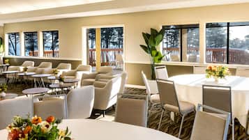 Habitación de hotel con un ventanal grande, zona de comedor con mesas y sillas redondas y vistas al exterior.