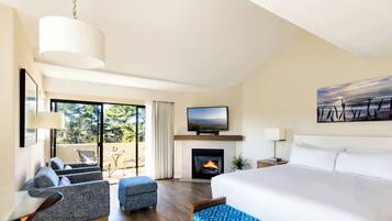 Una habitación de hotel moderna con una cama grande, un televisor de pantalla plana, una chimenea, un balcón con vista a árboles y un área de comedor con una mesa y sillas.