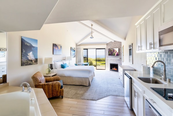 A modern hotel room with a large bed, a sitting area with a chair, a kitchen with a sink, and a fireplace. - Seascape Beach Resort (Aptos)