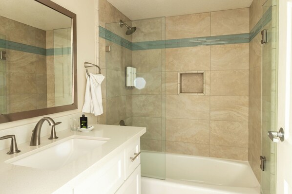 A modern bathroom with a double sink, a large mirror, a glass shower enclosure, and a bathtub.