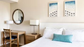 A hotel room with a bed, a desk with a chair, a nightstand with a lamp, a mirror, and two wall art pieces.