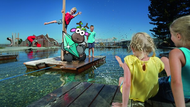 A wooden dock extending into a clear body of water with a playground structure featuring cartoon characters.