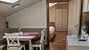 A compact room with a dining table, chairs, a bed, a TV, and a small kitchenette.