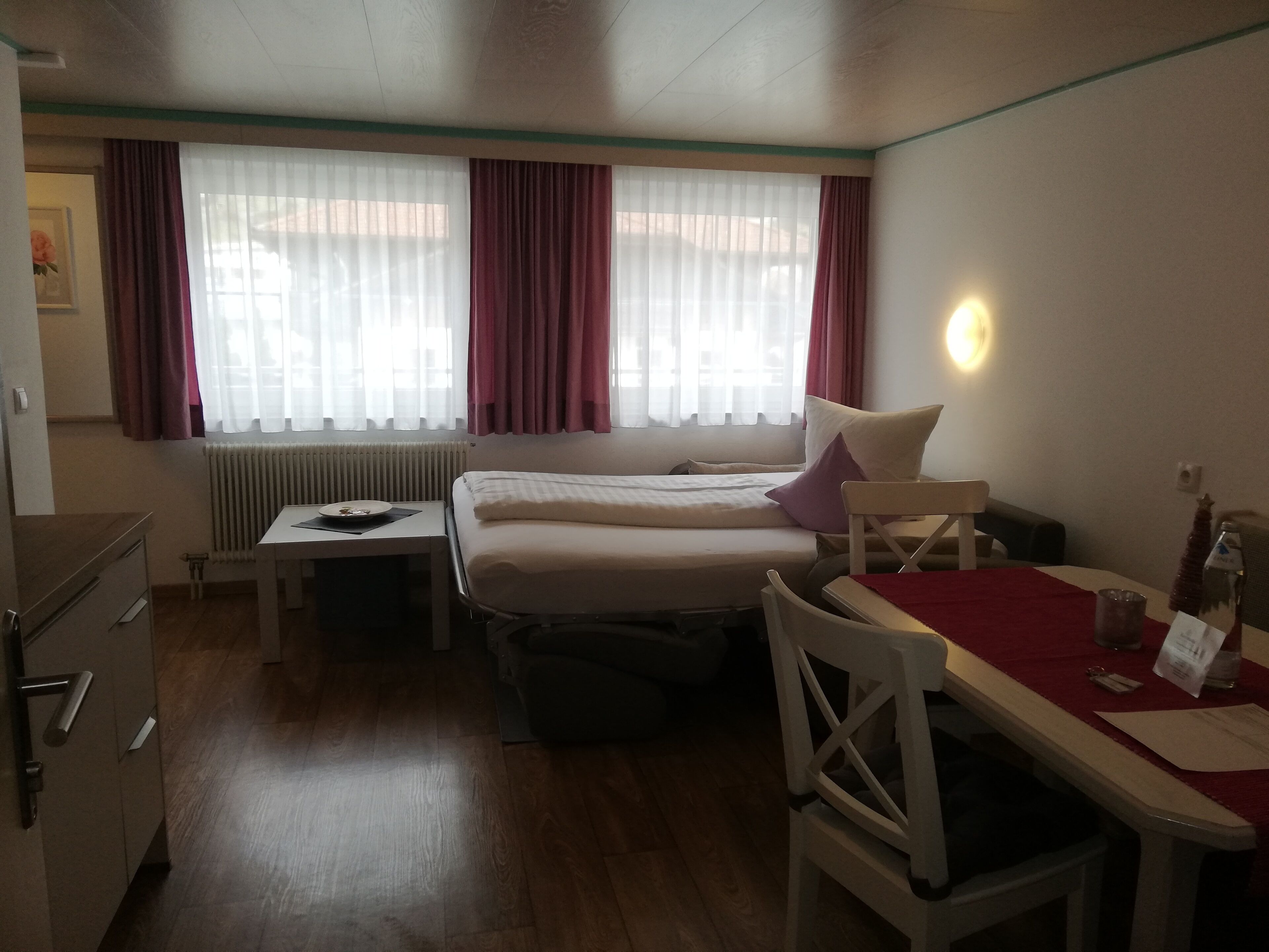Et lille hotelværelse med seng, et bord, en stol og en radiator.