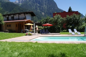 Zona de piscina con sillas de descanso, una parrilla y montañas al fondo.