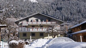 A multi-story building with a balcony, surrounded by snow-covered trees and mountains.