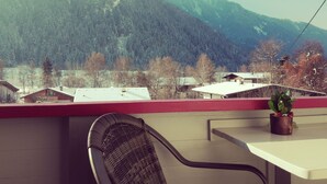 A balcony with a view of mountains and a small table with a chair.