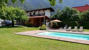 A pool area with a view of mountains, a wooden deck, and a building with a balcony.