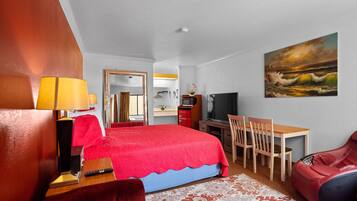 Une chambre d’hôtel avec un lit rouge, un bureau, une chaise, un fauteuil de massage, une télévision et un tableau représentant un paysage marin.