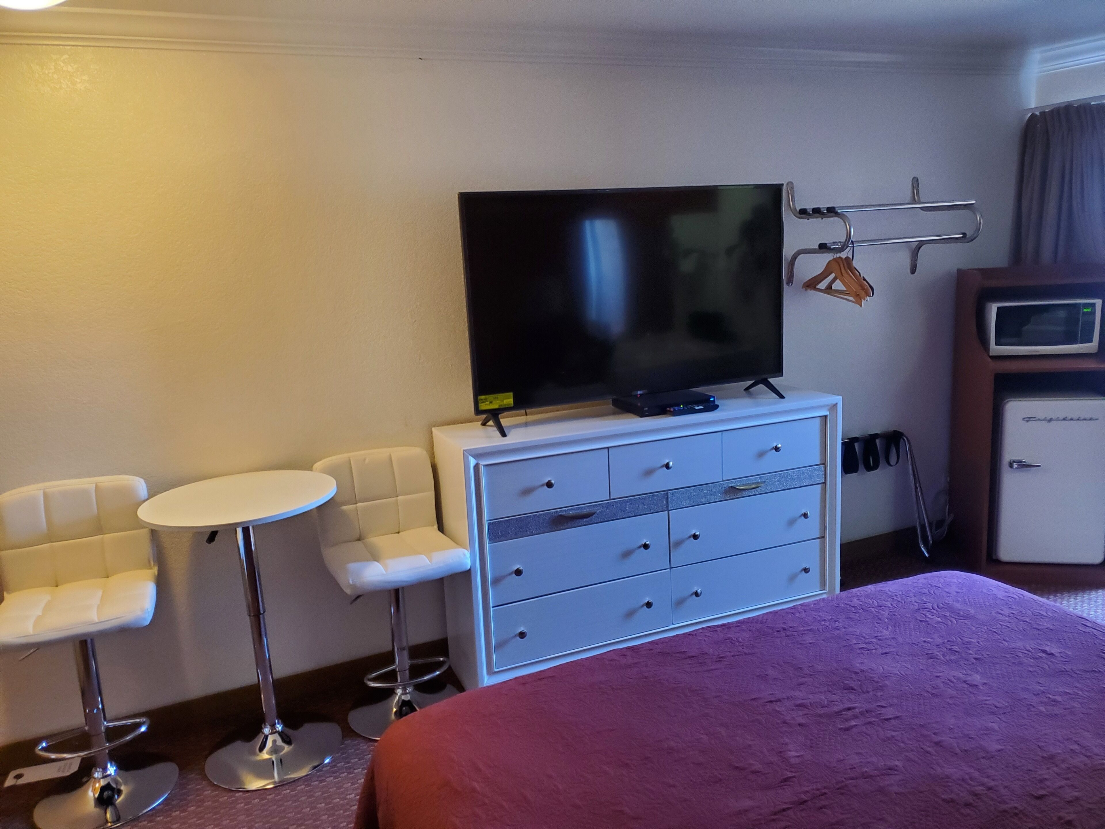 Hotelkamer met een bed, een televisie op een dressoir, twee witte stoelen, een bijzettafeltje en een minibar.