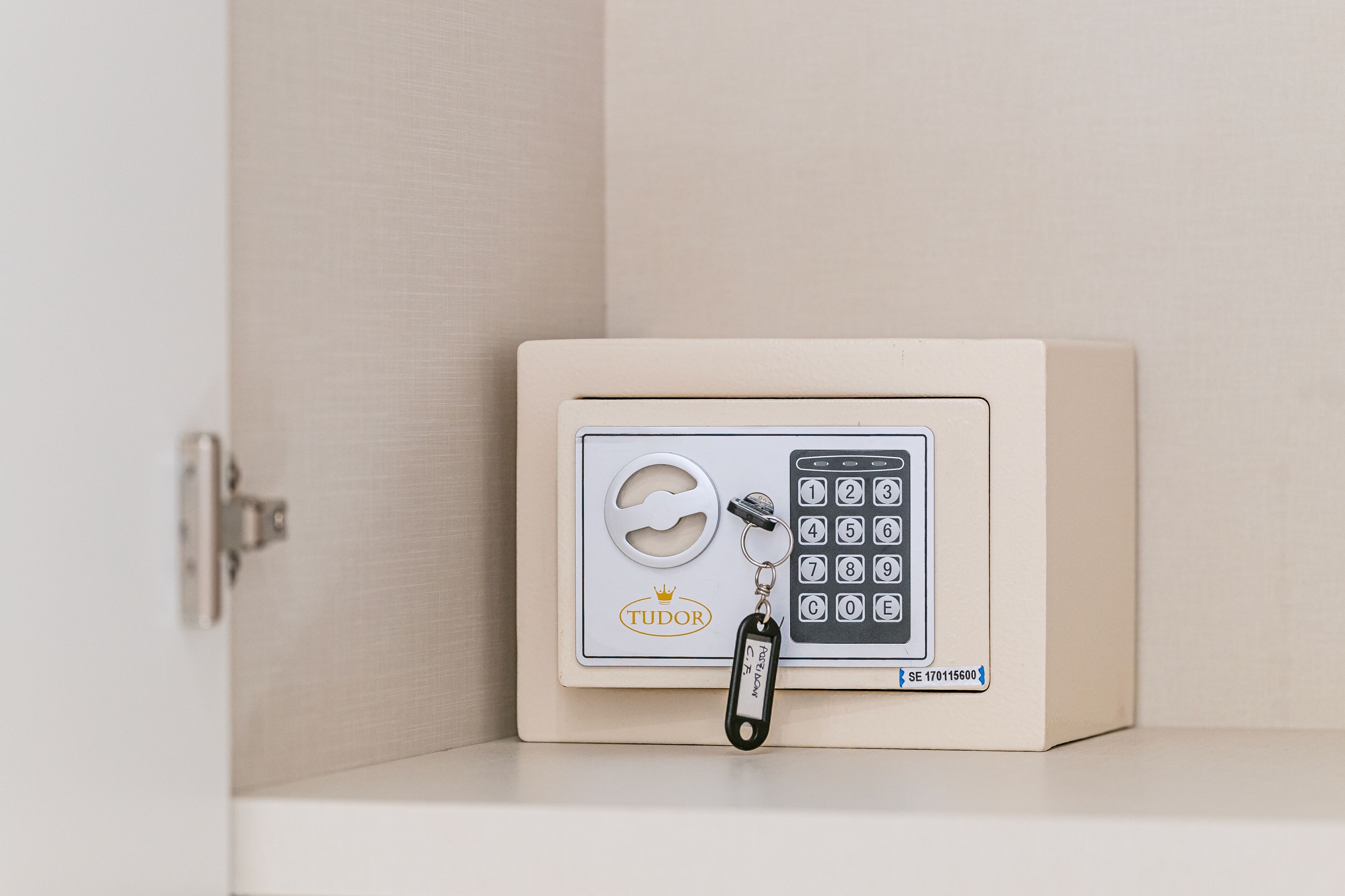 Een kluis met een keypad en sleutelhanger, geplaatst op een plank tegen een muur.