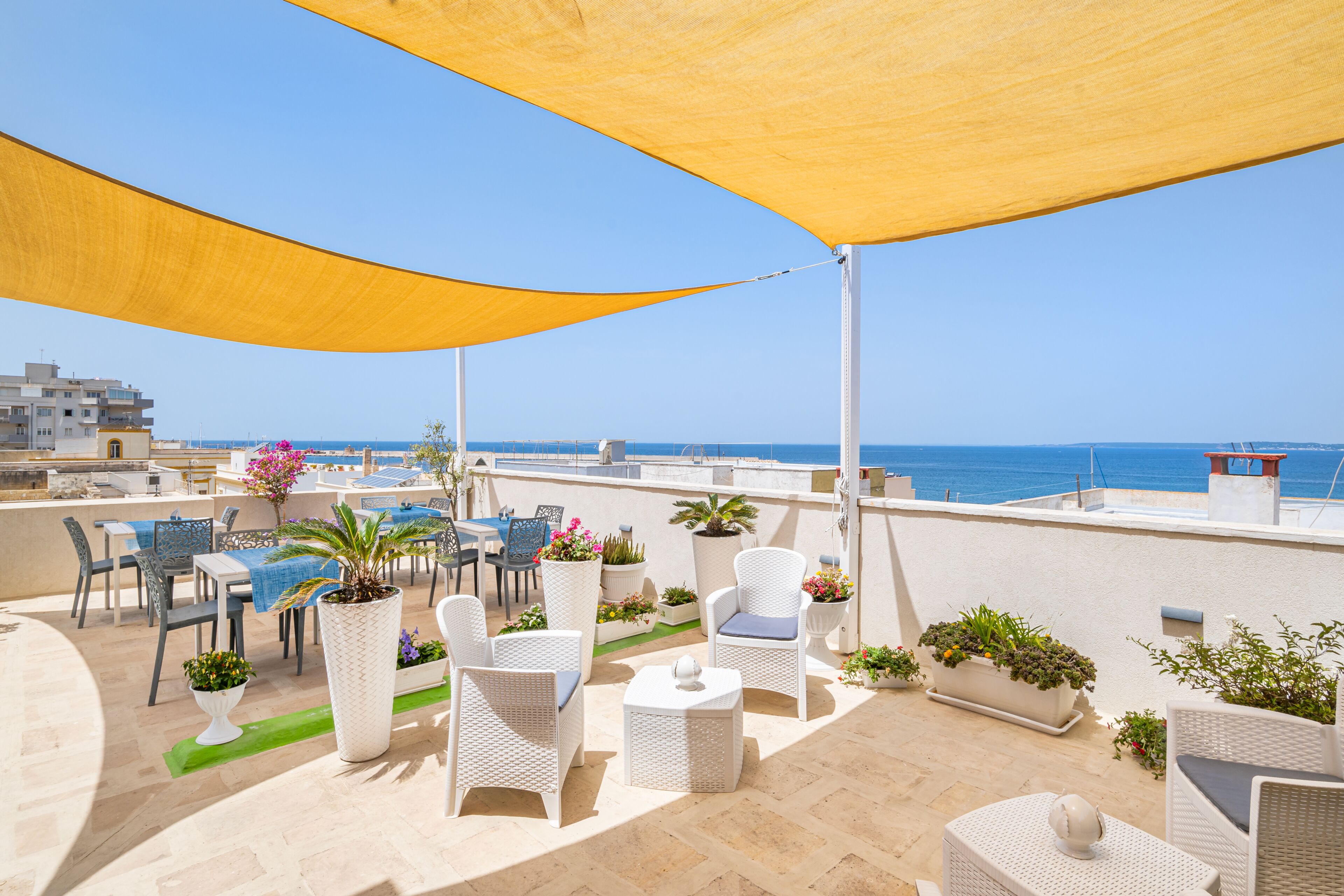 A rooftop terrace with outdoor seating, potted plants, and a view of the sea.