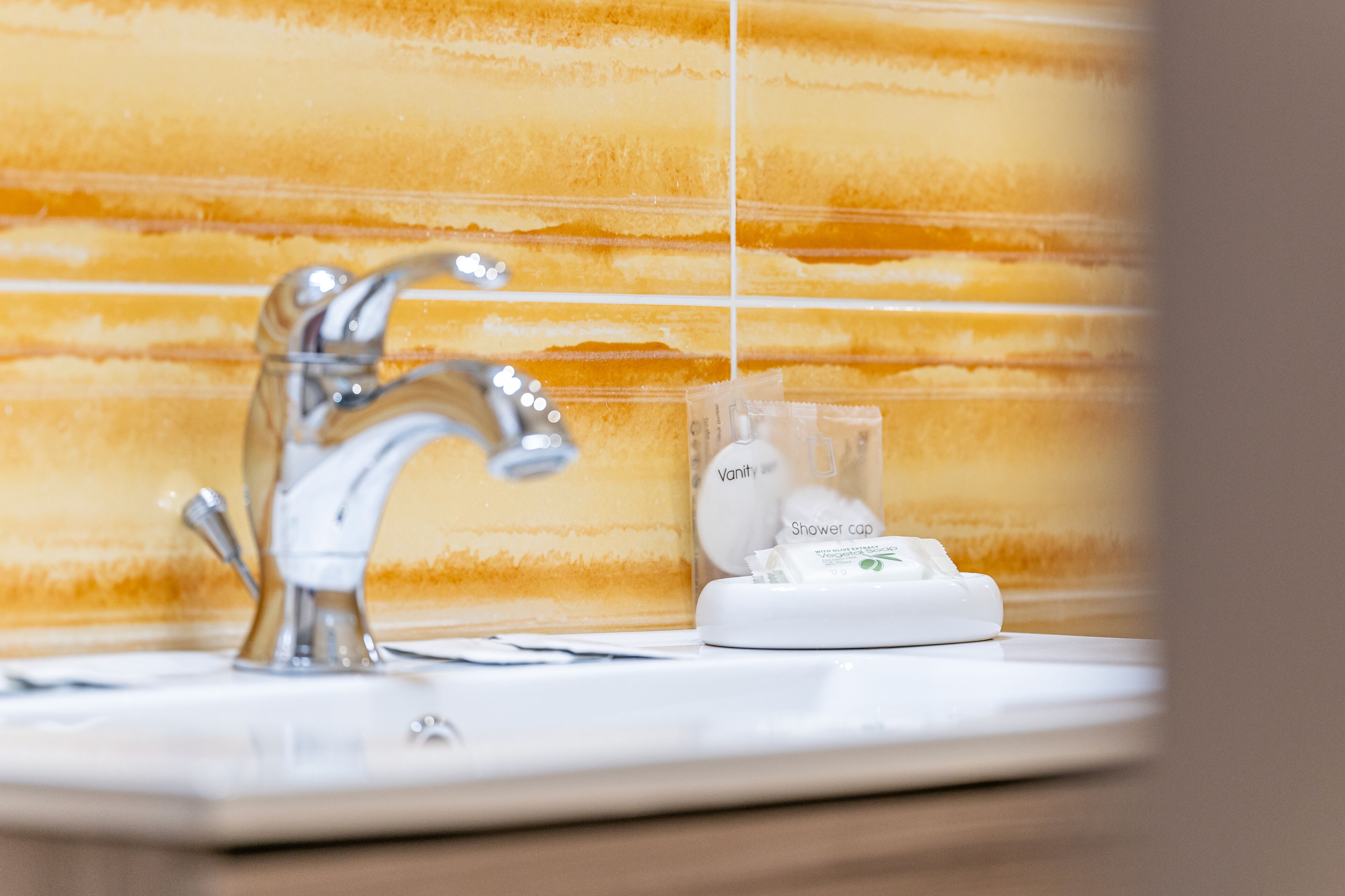 A bathroom with a modern faucet, a shower cap, and a bottle of shampoo.