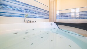 Un baño moderno con una bañera acristalada, un cabezal de ducha y una pared con un diseño abstracto azul y blanco.