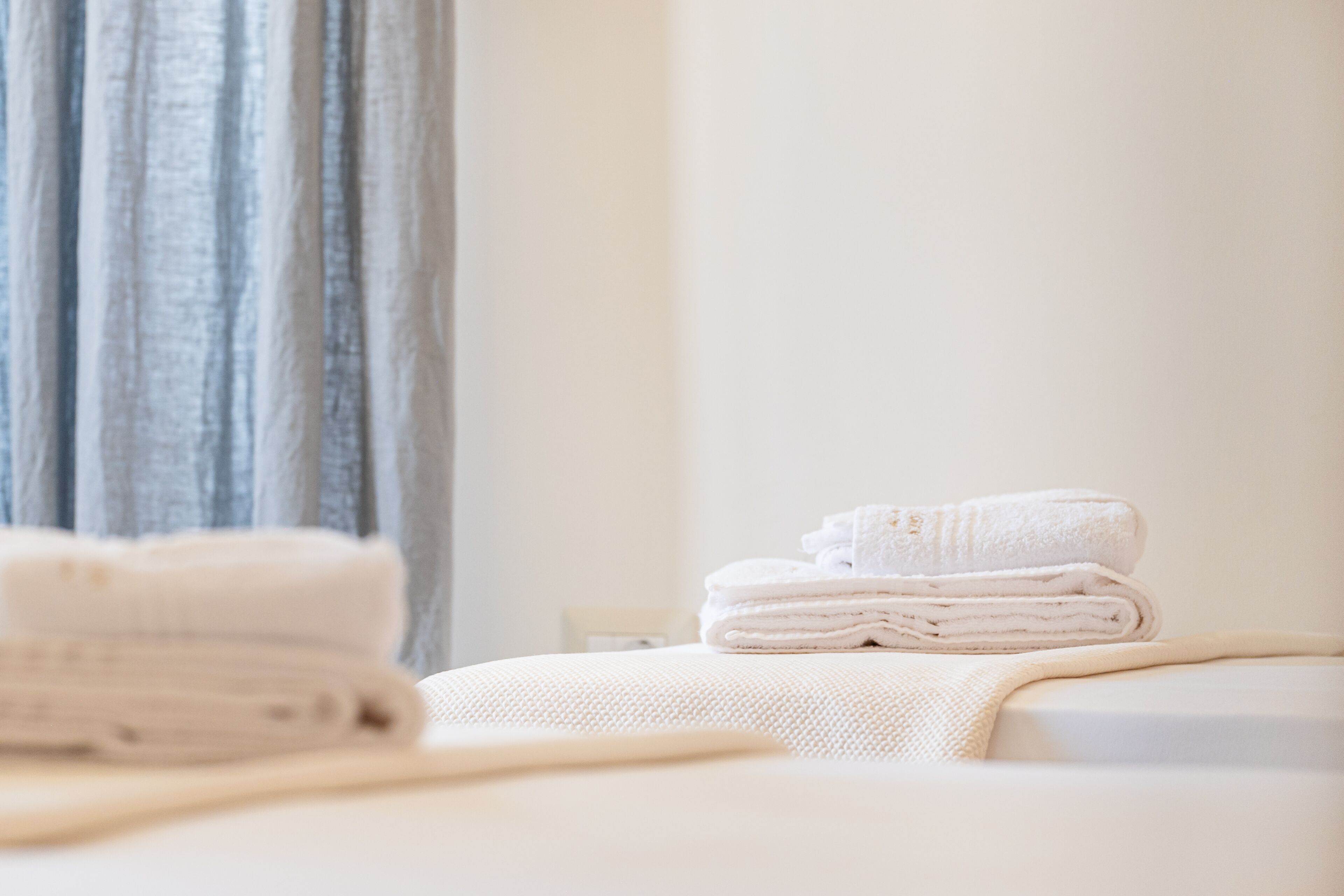 Un lit bien fait, avec des serviettes blanches pliées et une couverture beige.