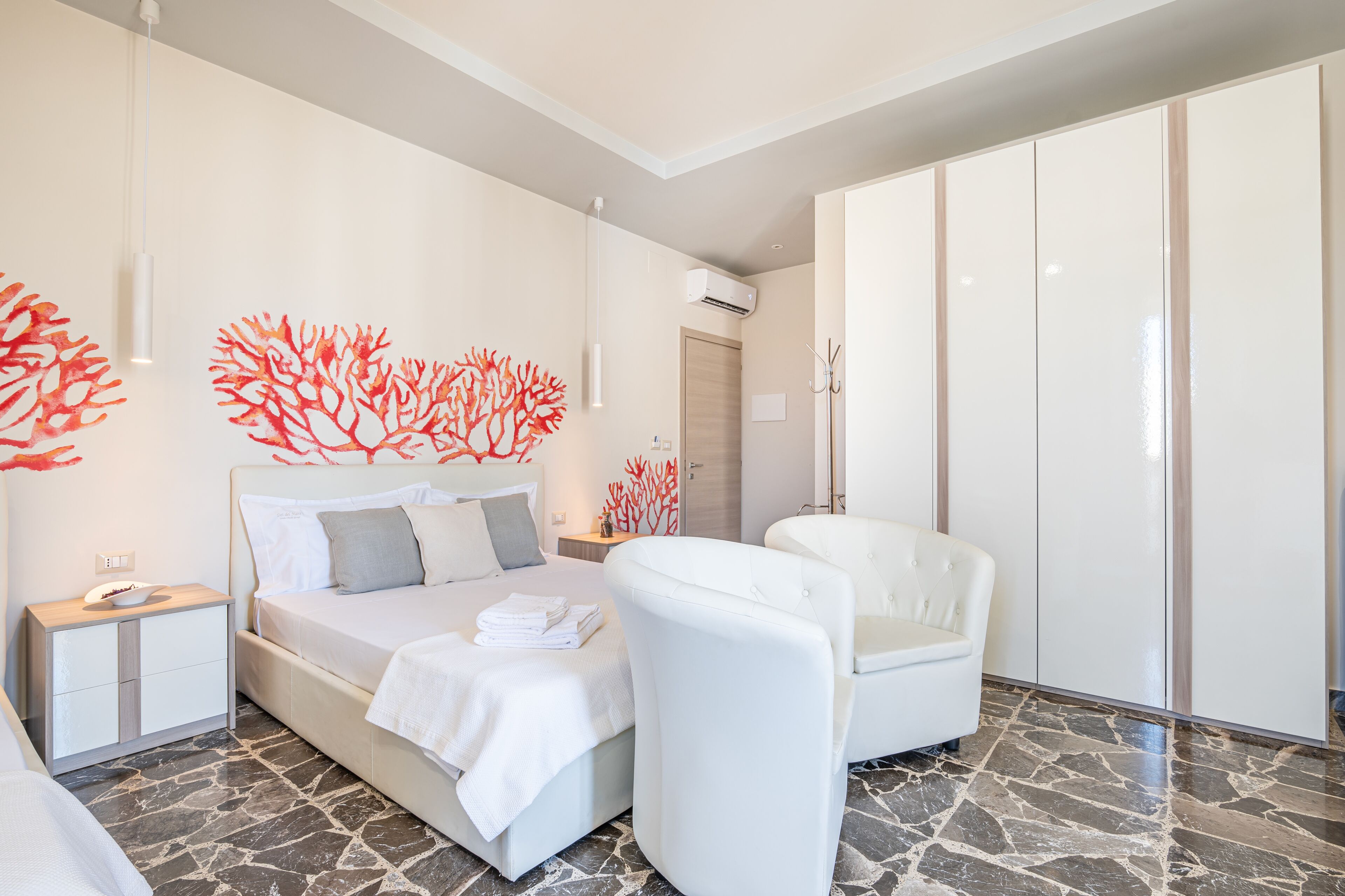 A modern bedroom with a bed, a white chair, a nightstand, and a wardrobe.