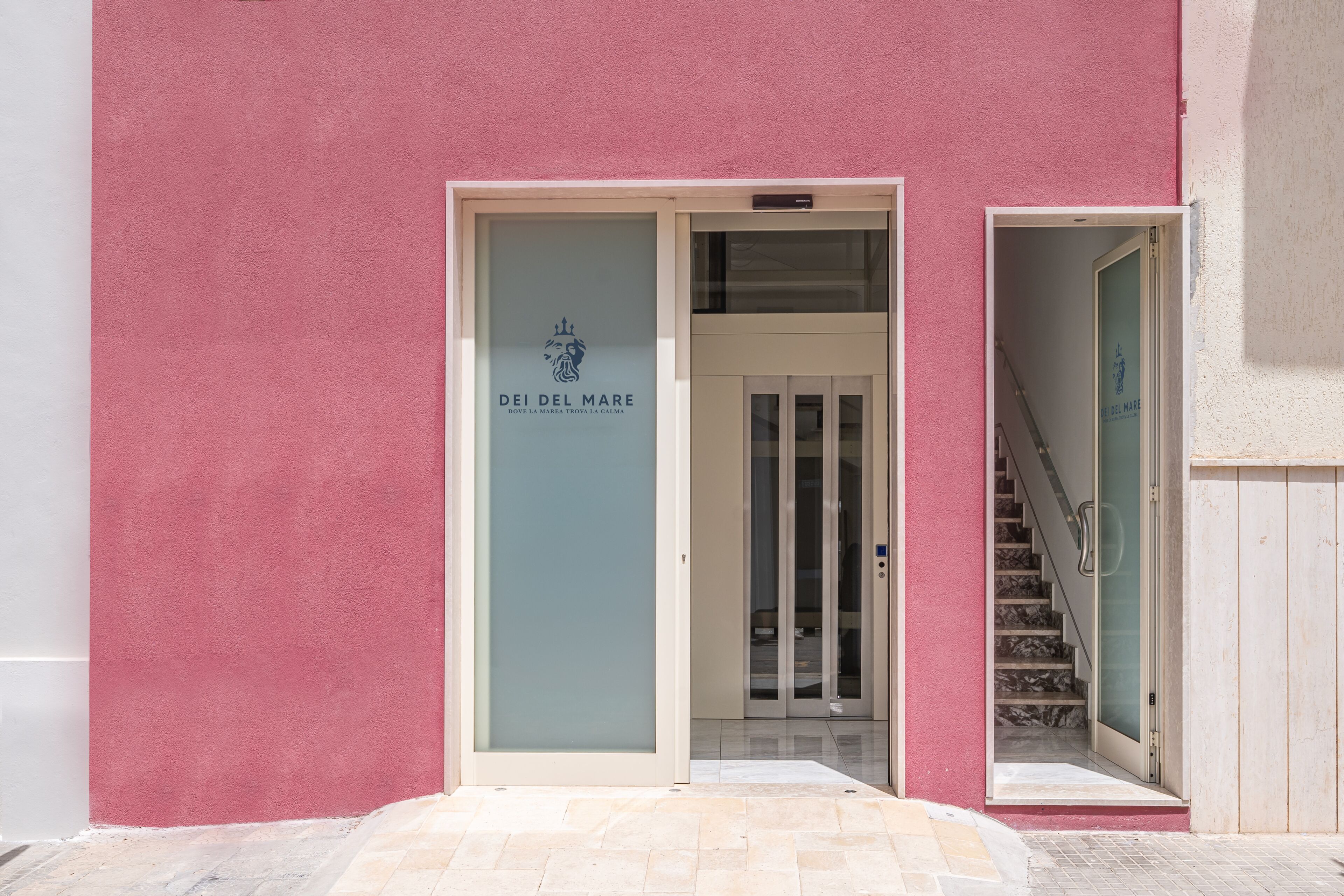 Entrada de un edificio con puerta de vidrio, una escalera y un letrero que dice 'DEI DEL MARE'.