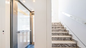 Un interior moderno con una escalera de mármol, una puerta de ascensor de vidrio y un suelo cubierto de alfombra azul.