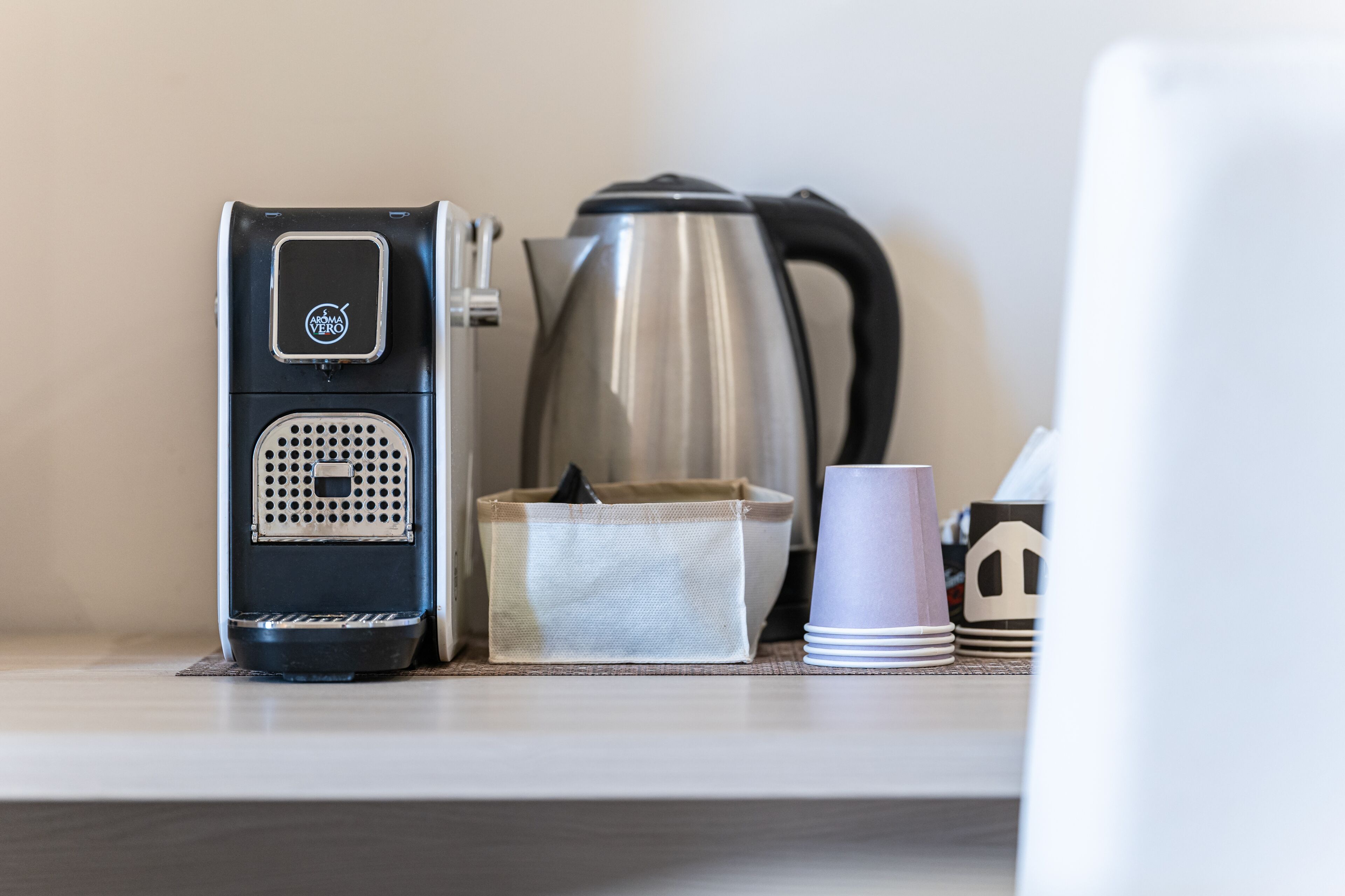 A coffee maker, a kettle, and a stack of cups on a table.