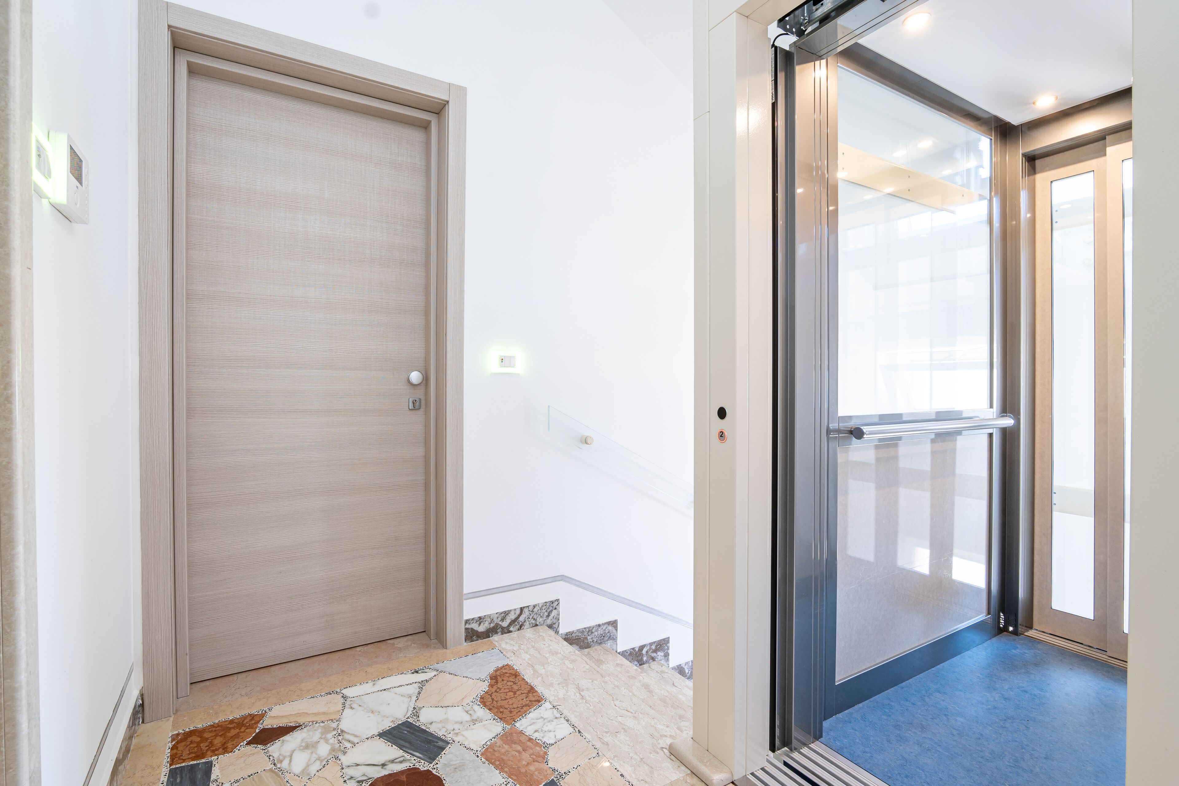 Un pasillo con una puerta de madera, una puerta de ascensor de vidrio y un suelo estampado.