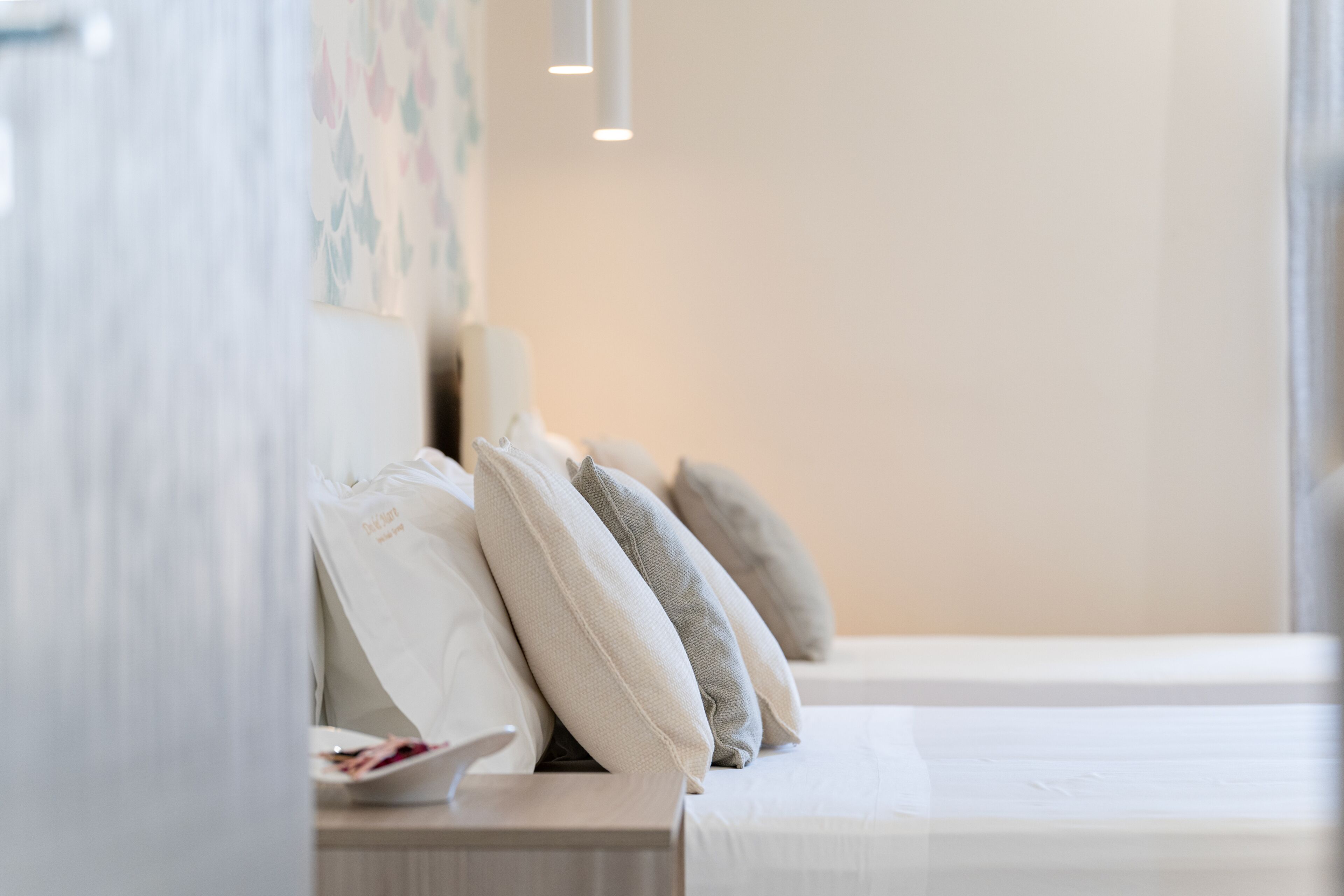 A neatly arranged bed with pillows, a bedside table with a plate and a bag, and a wall with a floral pattern.