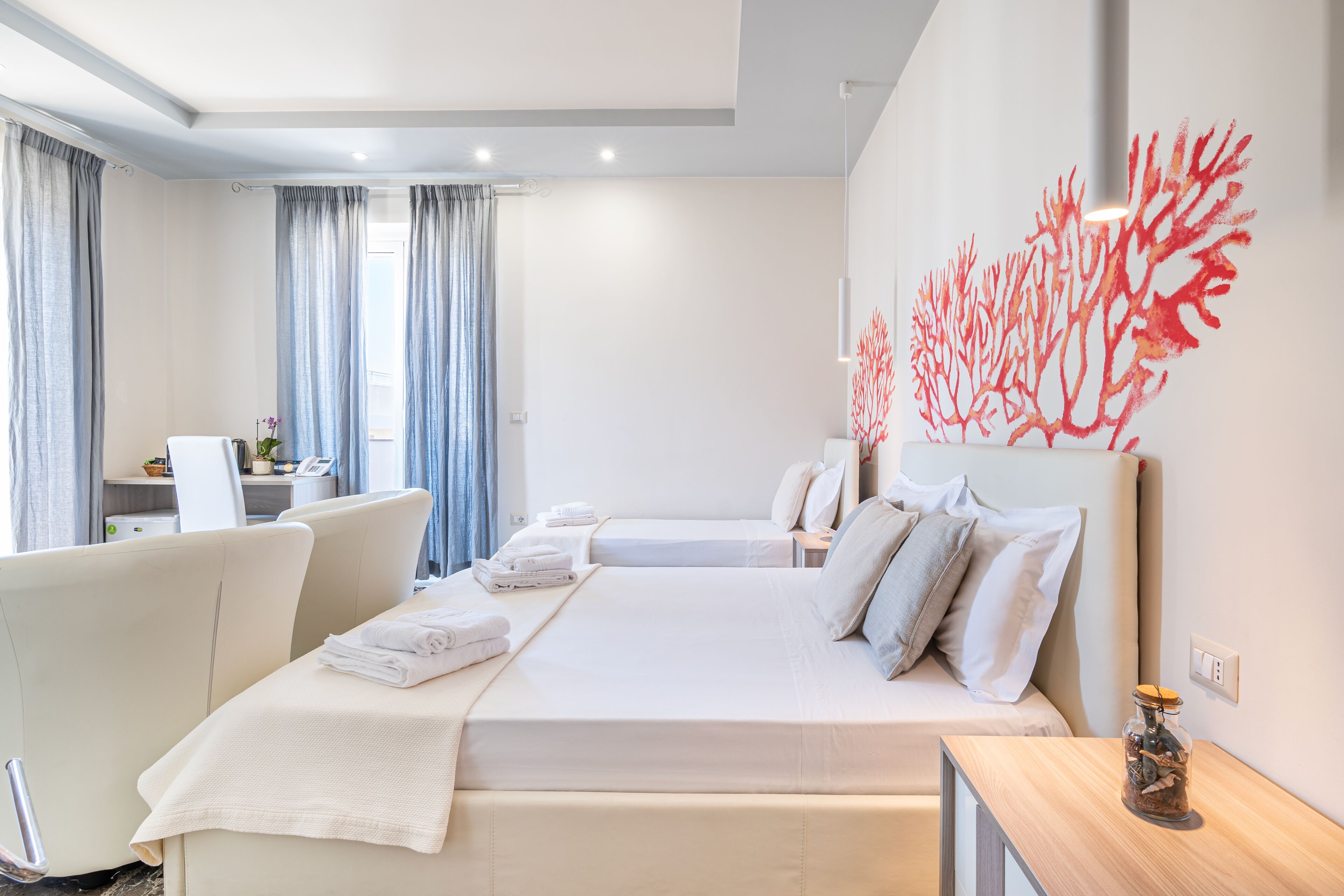 A modern hotel room with a bed, bedside tables, a desk, and a large window with curtains.