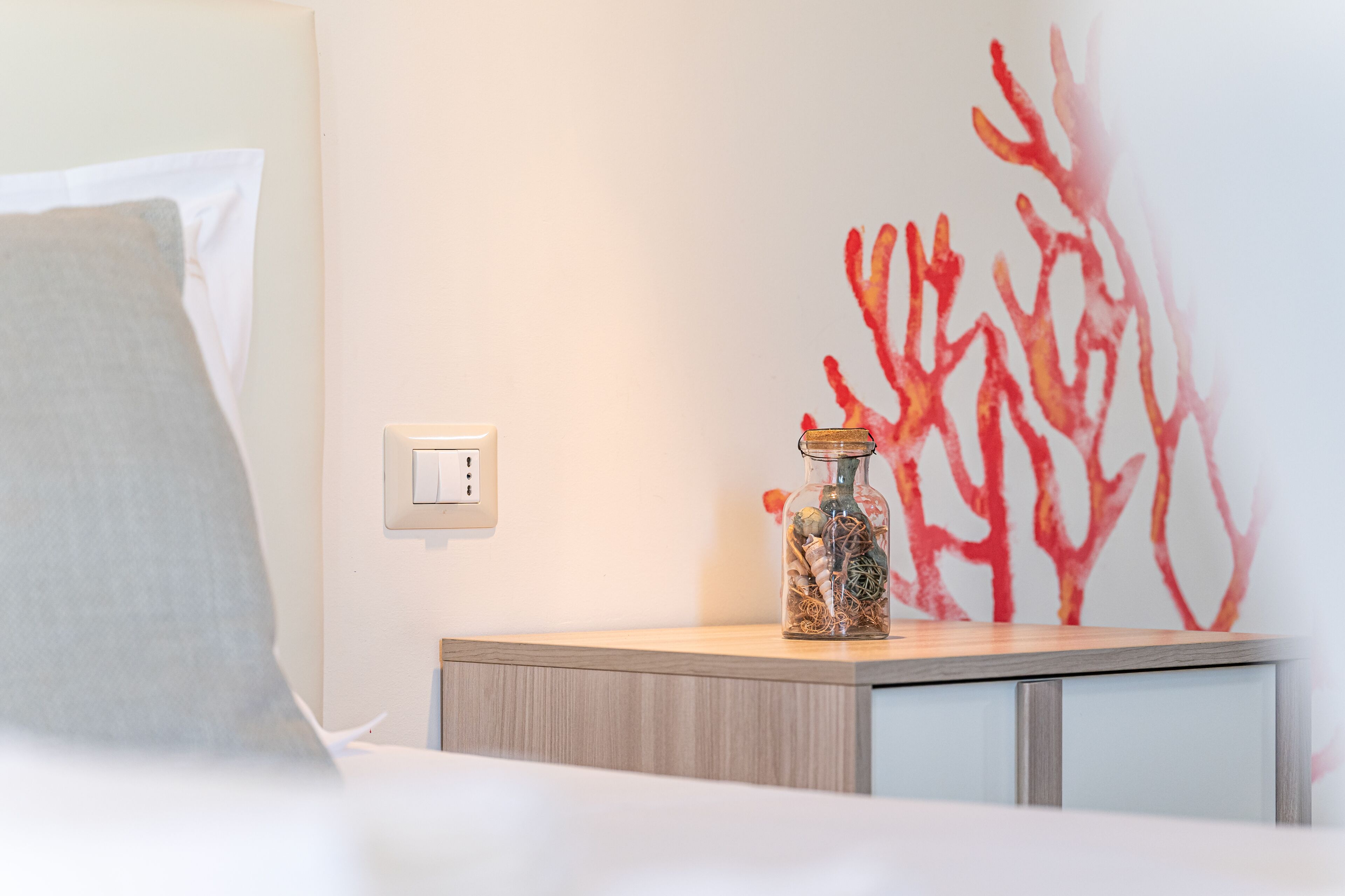 A bed with a pillow, a bedside table with a glass jar, and a wall with abstract red artwork.