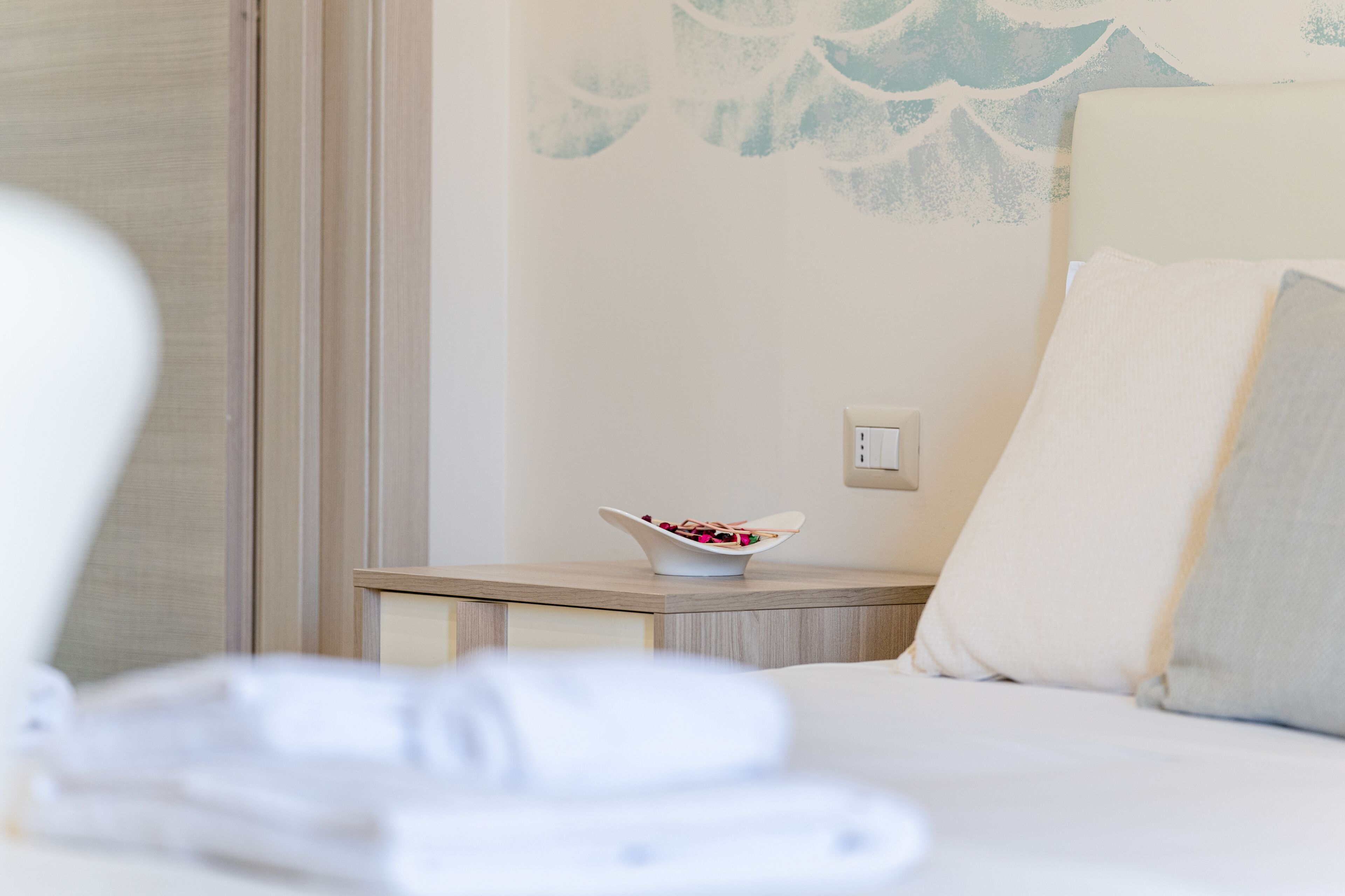 A hotel room with a bed, a bedside table with a bowl of fruit, and a wall with a floral pattern.