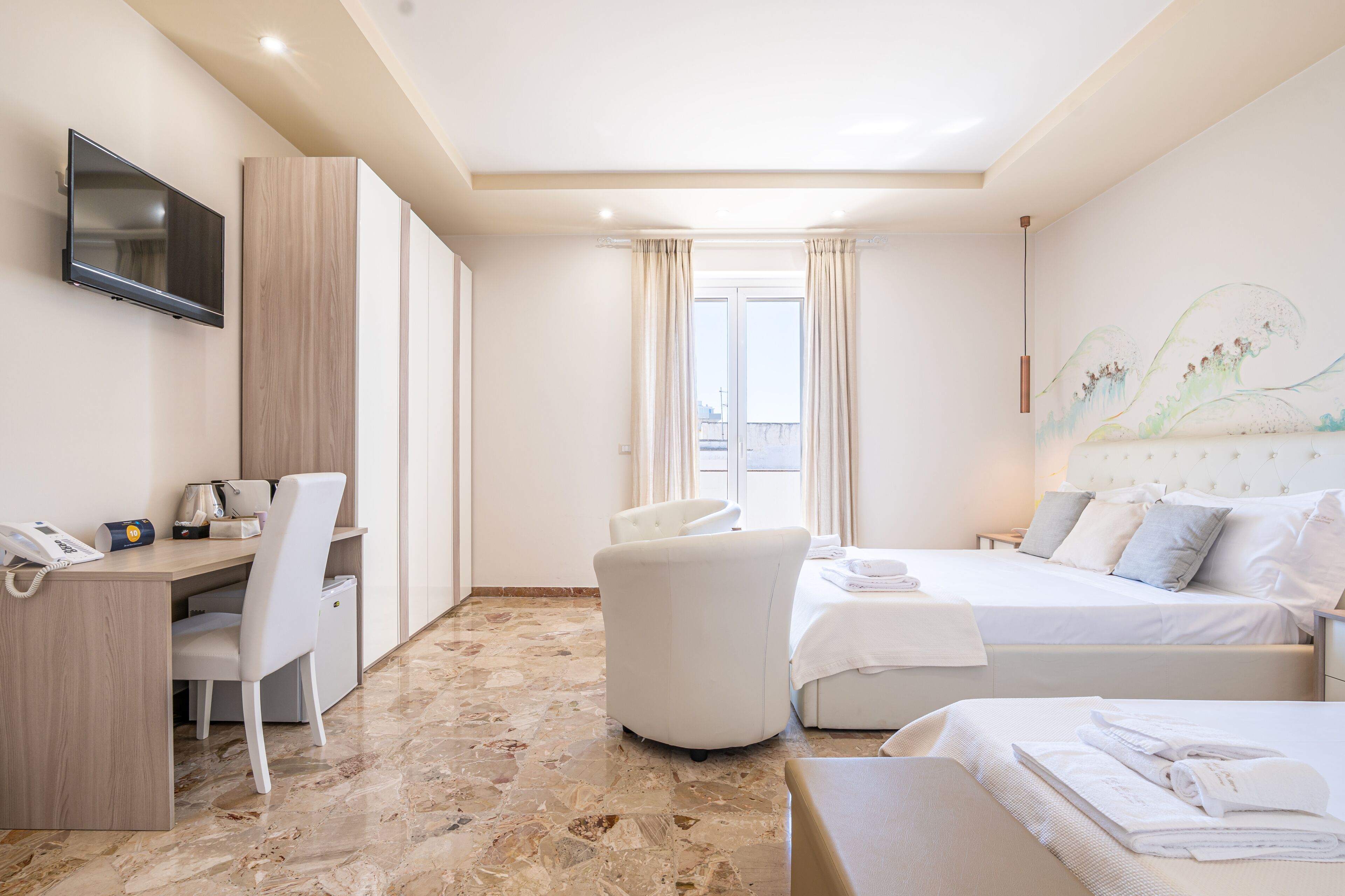 Ein Hotelzimmer mit Schreibtisch, Stuhl, zwei Betten, Fernseher und einem großen Fenster mit Vorhängen.