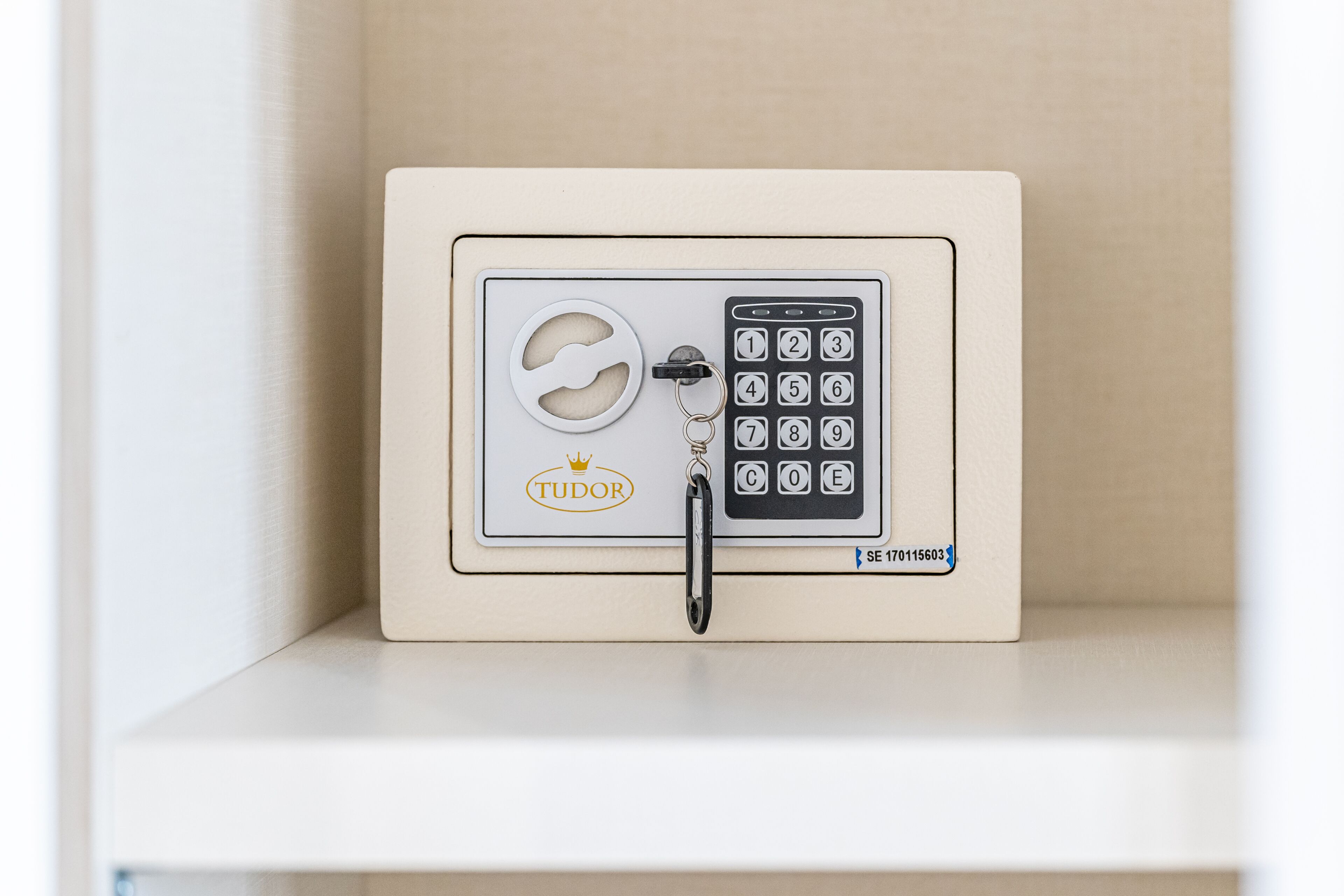 A safe with a keypad and a keyring, labeled 'TUDOR,' on a shelf.