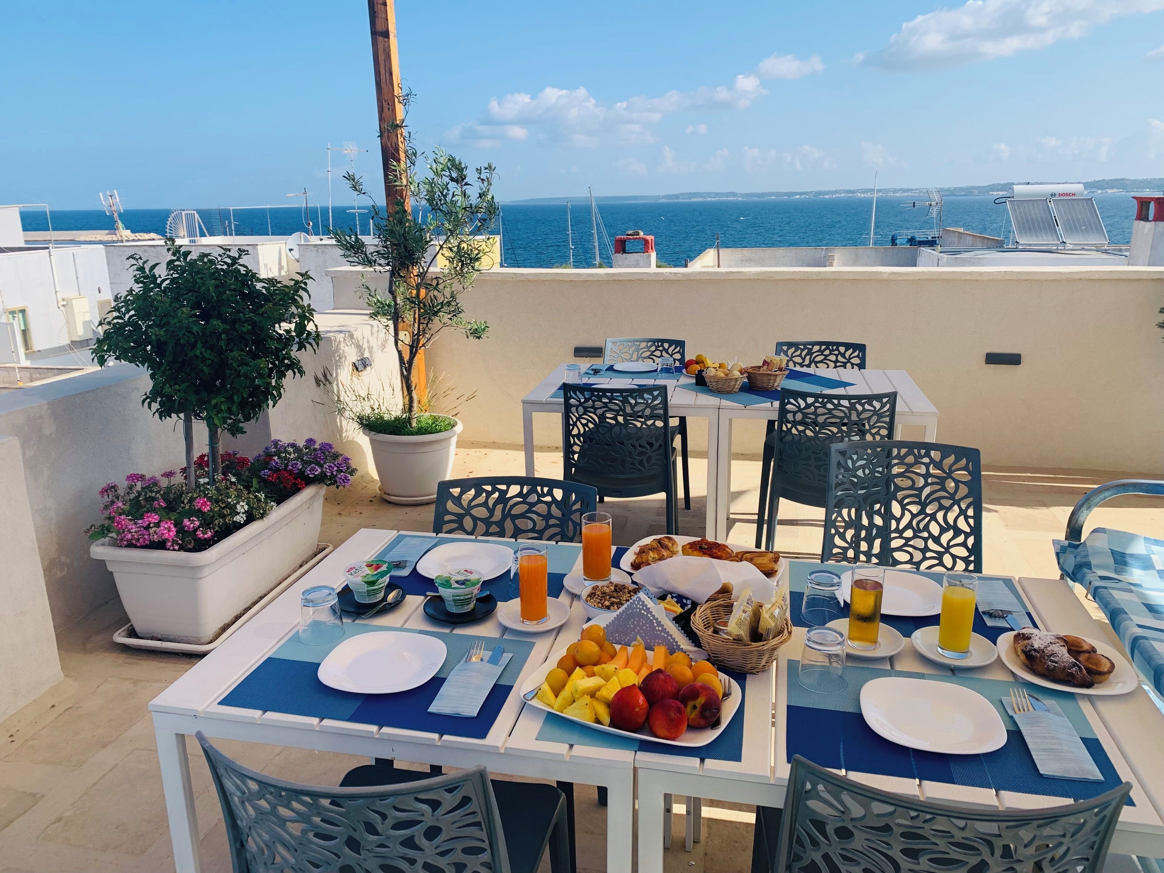 Un espace de restauration aménagé sur le toit, avec des tables préparées pour le petit-déjeuner, offrant une vue sur la mer.