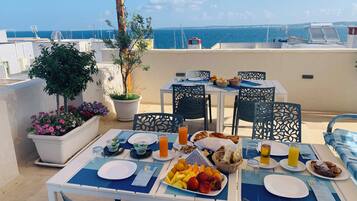 Un espace de restauration aménagé sur le toit, avec des tables préparées pour le petit-déjeuner, offrant une vue sur la mer.