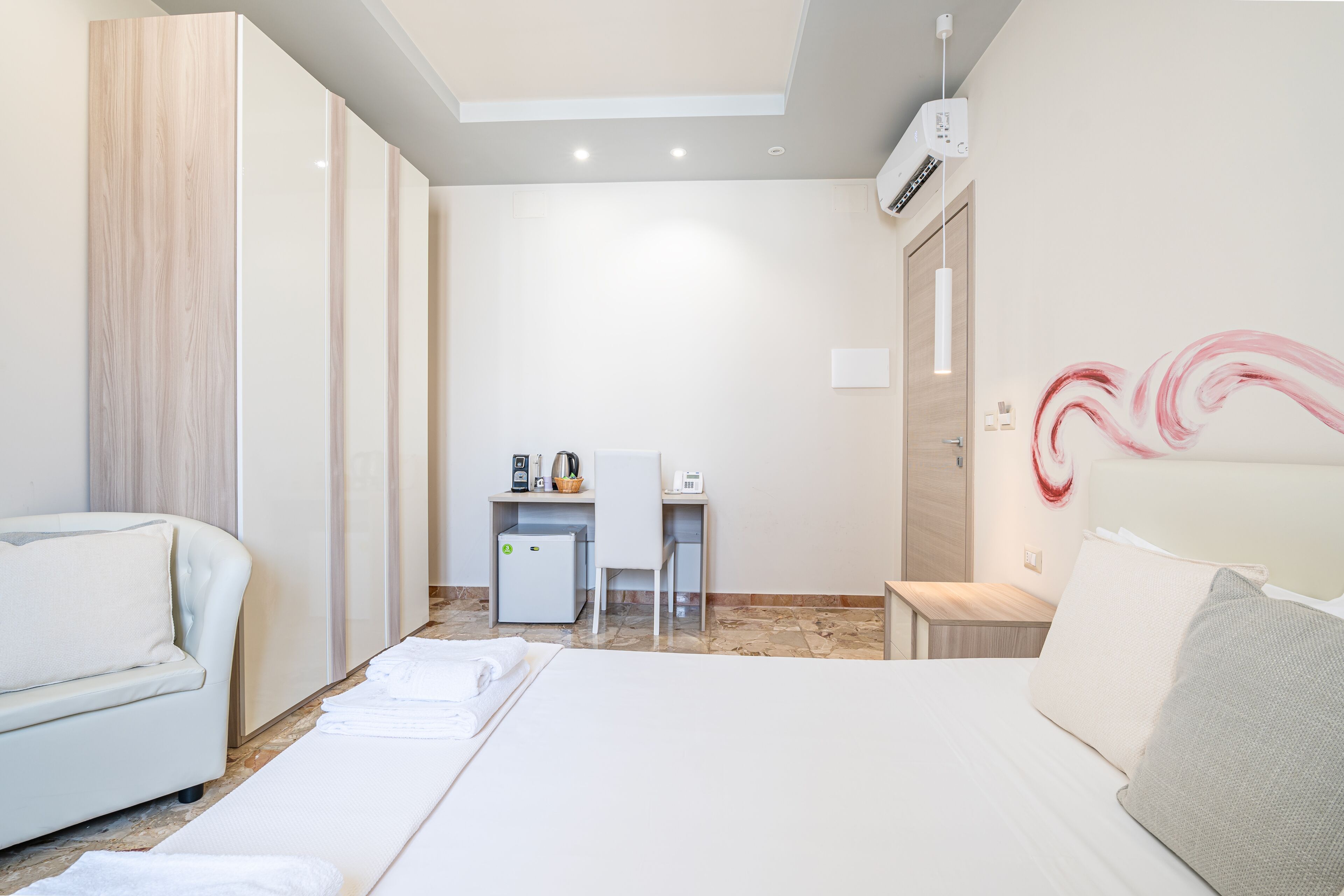 Ein Hotelzimmer mit Bett, Schreibtisch, Stuhl, Kleiderschrank und einem Wandbild.
