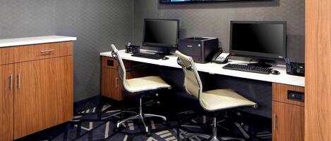A modern office space with two desks, two chairs, and a large screen on the wall.