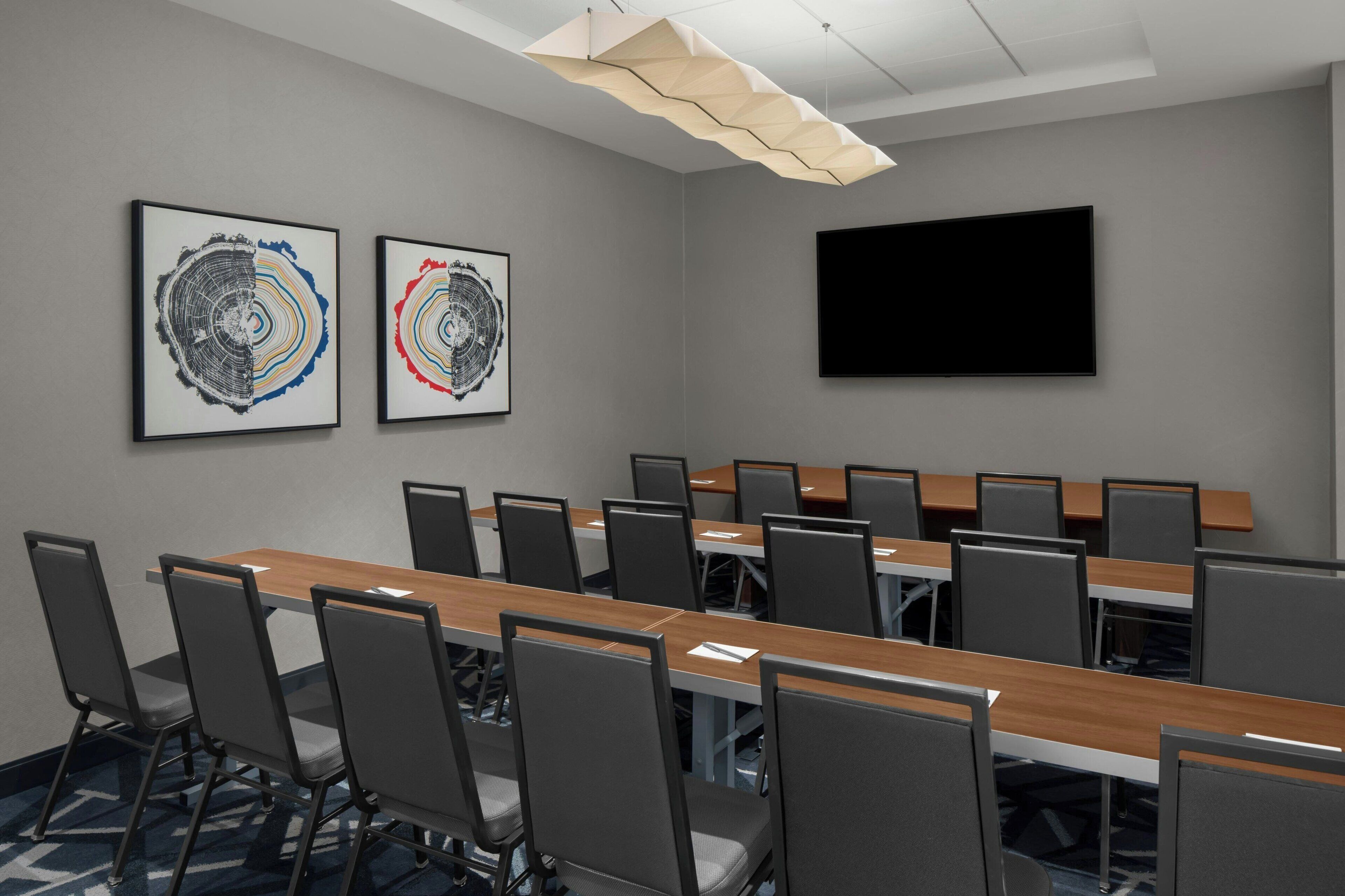 A conference room with a long table, chairs, a flat-screen TV, and two framed artworks on the wall.