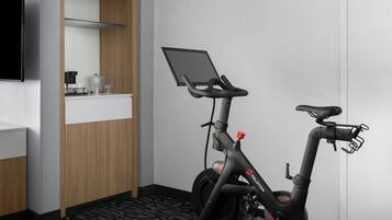 Quarto de hotel moderno com bicicleta ergométrica, TV de tela plana e pequena área de cozinha.