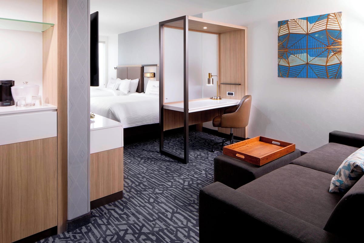 A hotel room with a bed, a desk, a chair, a sofa, a coffee maker, and a tray.