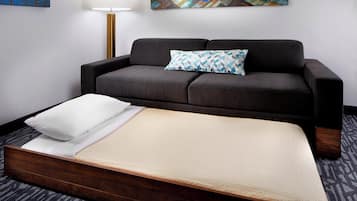 Una habitación de hotel moderna con sofá, una cama individual, una lámpara y arte abstracto en las paredes.