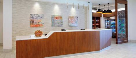 A reception desk with a wooden finish, three abstract paintings on the wall, and a modern lighting fixture above.