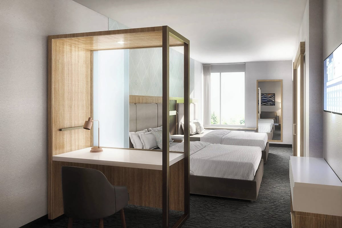 A modern hotel room with a desk, two beds, a large mirror, and a view of the city.