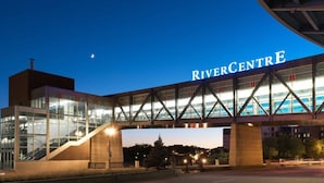 Un edificio moderno con el nombre "RiverCentre" bien visible. Cuenta con fachada de vidrio, un acceso cubierto y una escalera que lleva al nivel superior.
