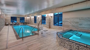 Una piscina interior moderna con jacuzzi, suelo de baldosas y grandes ventanales con vistas.