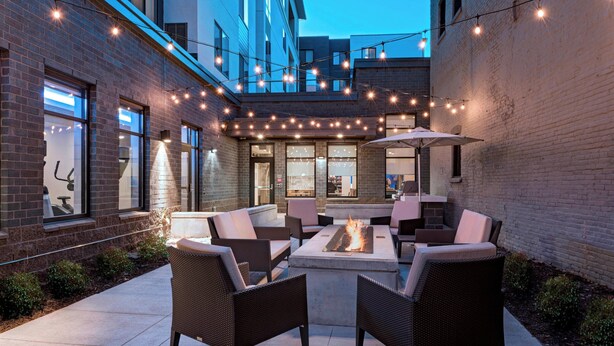 Un patio al aire libre con mobiliario de mimbre, un hogar de fuego y luces colgantes.