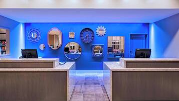 Un espace d’accueil doté de deux comptoirs, d’un mur bleu orné de miroirs décoratifs et d’horloges, et d’un sol recouvert de moquette.